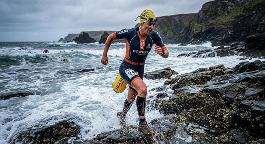 A professional Swim-Runner sprinting out of a cold, rocky ocean entry during a high-stakes endurance event.