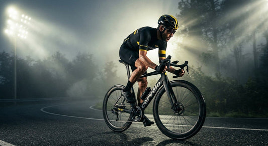 A professional cyclist in a focused aerodynamic position riding on a foggy morning road with dramatic stadium-style lighting