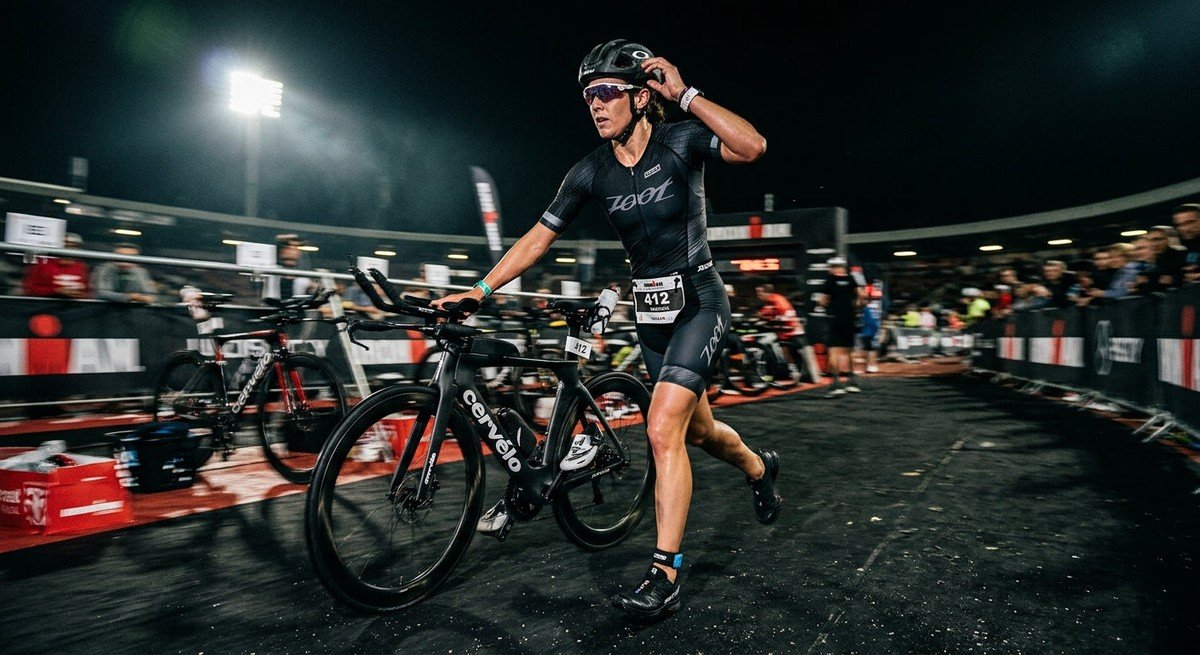 A triathlete performing a high-speed transition from a bike to a run in a moody stadium setting with cinematic lighting and motion blur