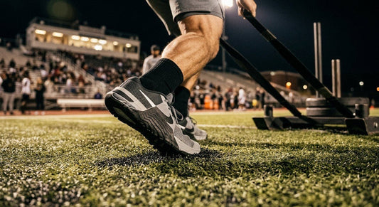 A close-up shot of an athlete's high-performance trainer gripping the textured turf during a heavy sled pull with cinematic stadium lighting.