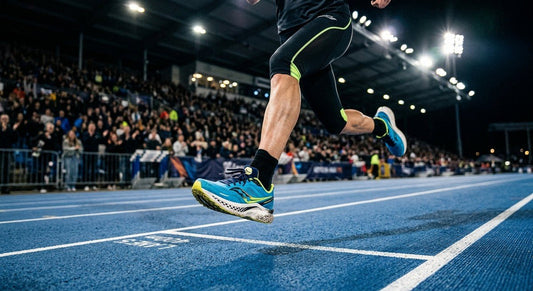 A professional action shot of a runner's feet mid-stride on a synthetic track, featuring the Saucony Endorphin Speed 4 with motion blur and dramatic stadium lighting.
