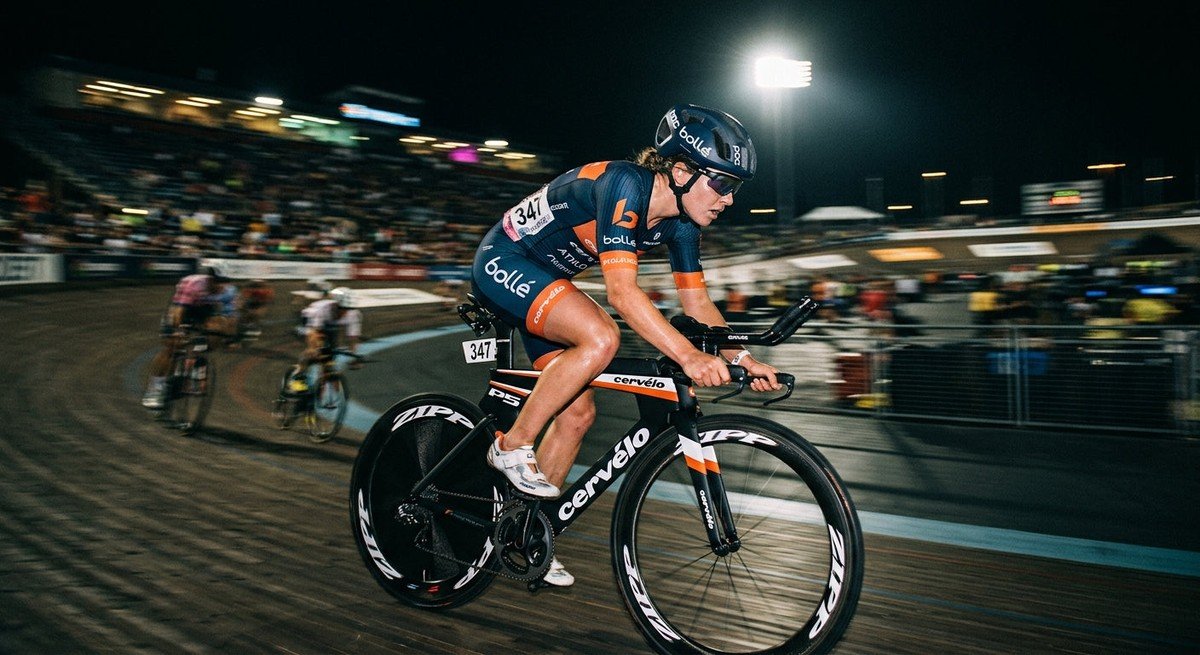 A professional triathlete wearing high-performance Bollé sunglasses during a high-speed cycling sprint, captured with motion blur and dramatic stadium lighting.