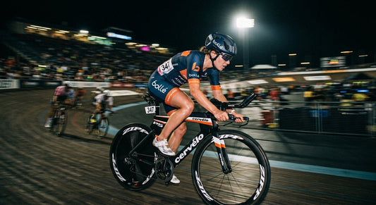 A professional triathlete wearing high-performance Bollé sunglasses during a high-speed cycling sprint, captured with motion blur and dramatic stadium lighting.
