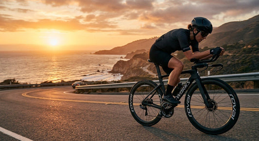Professional cyclist in an aerodynamic tuck position on a road bike using sleek black clip-on aerobars during a sunset training session