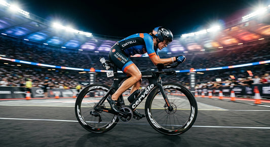 A professional triathlete in an aerodynamic position on a carbon road bike, captured with dramatic stadium lighting and high-speed motion blur.