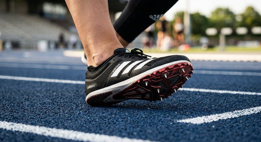 A close-up of a professional athlete wearing Adidas Adizero Ambition spikes, highlighting the textured material and aggressive spike plate design on a professional synthetic track.