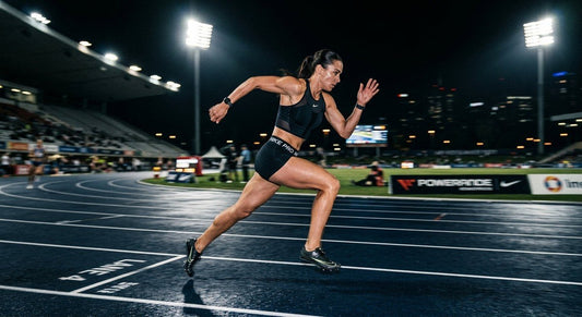 A professional runner sprinting on a dark track at night with cinematic stadium lighting and dramatic motion blur.