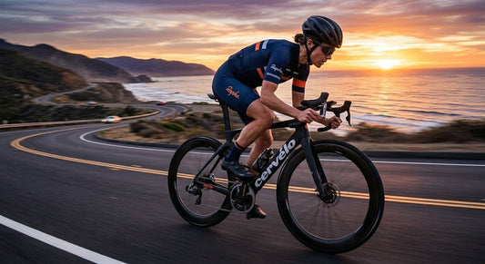 A professional cyclist in a sleek aero kit riding a carbon road bike at high speed during a sunset, with a clear focus on the mounted flagship bike computer.