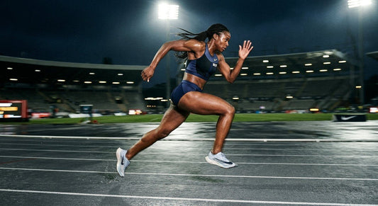 A professional athlete sprinting on a dark, dramatic stadium track with intense motion blur highlighting explosive leg drive.