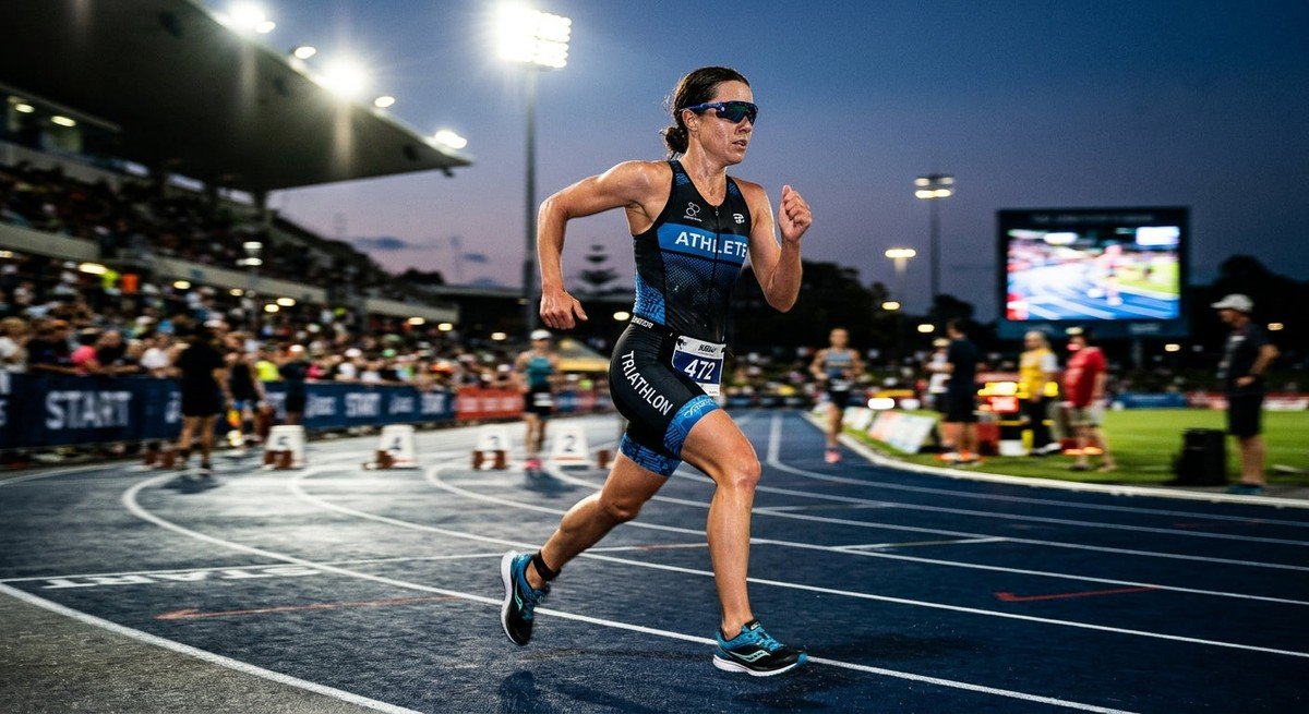 A professional high-speed action shot of a triathlete running in intense stadium lighting, wearing sleek performance sunglasses with motion blur.