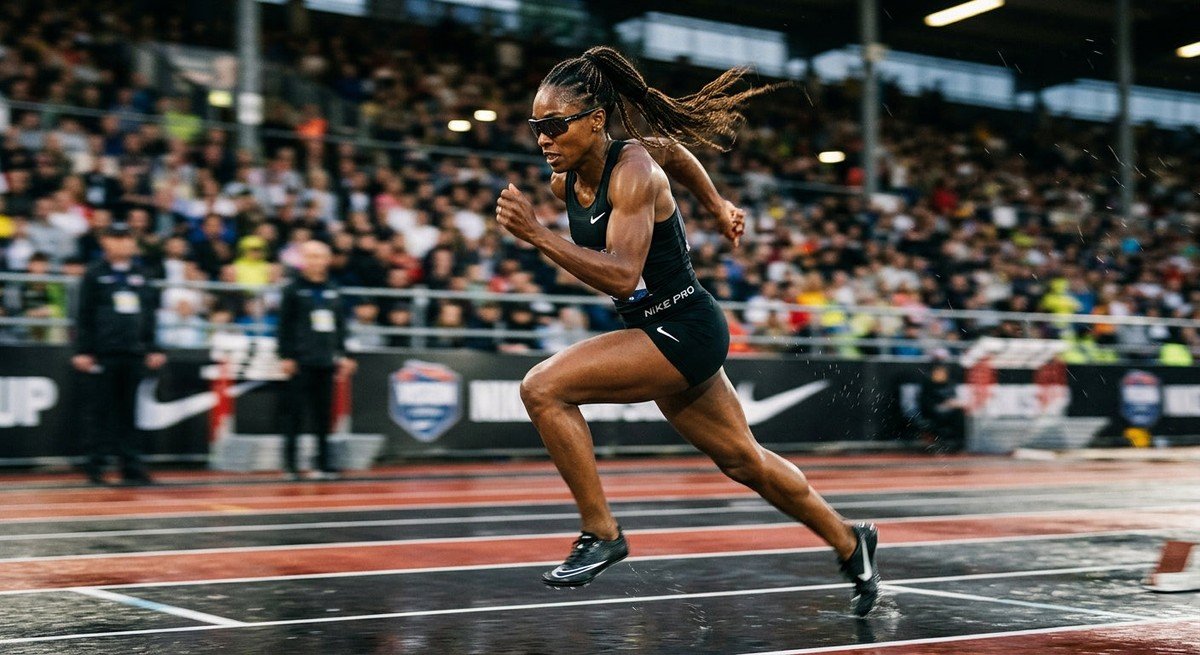 A professional athlete wearing Nike Vision Prima Arc sunglasses during an intense sprint in a stadium, featuring motion blur and dramatic lighting.