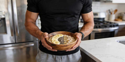 A full length photo of a fit male athlete in a modern kitchen holding a healthy bowl of high fibre porridge and fresh fruit.