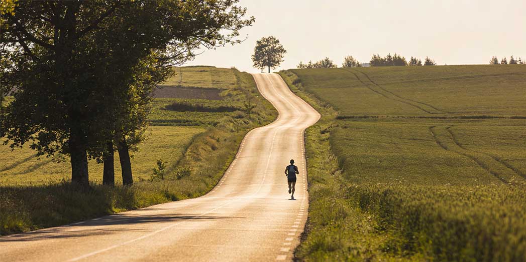 A full length view of a runner heading down a long open road representing the path from a 5k to a marathon.