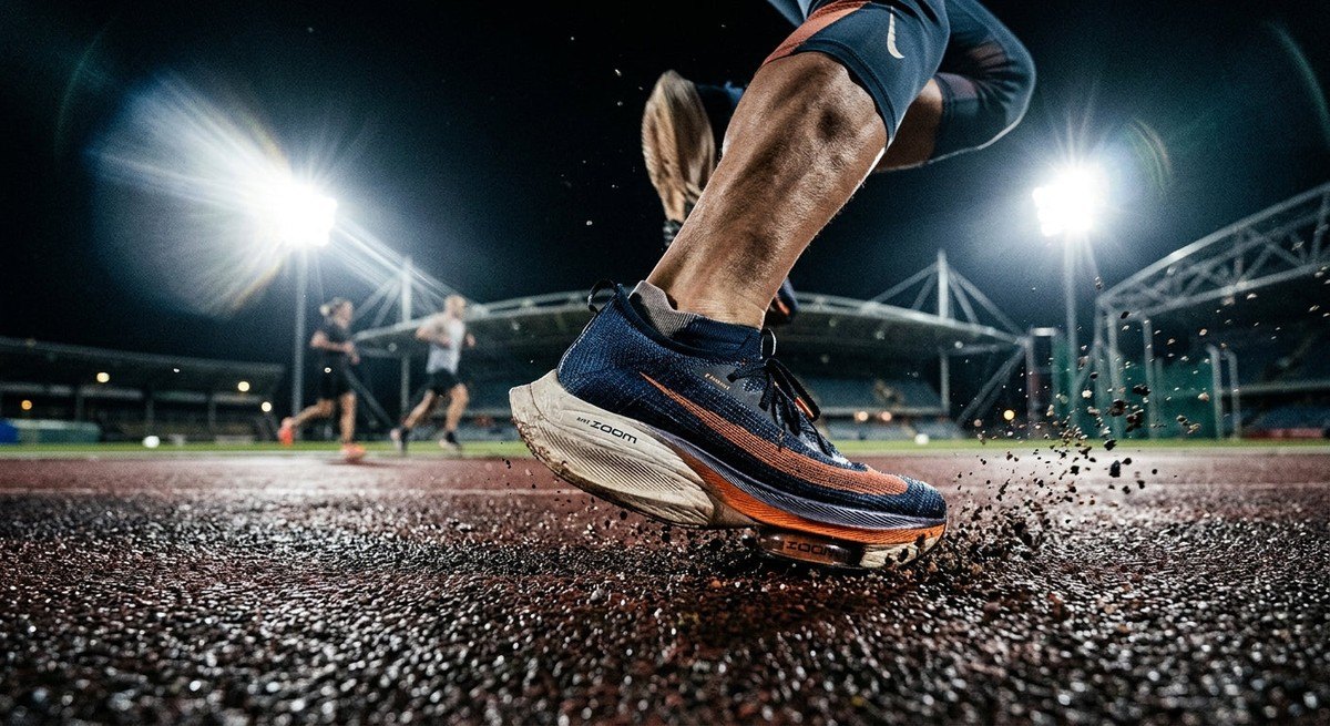 A close-up, dramatic image of a runner's shoe making contact with the ground during a workout, showcasing technical cushioning and stadium lighting.