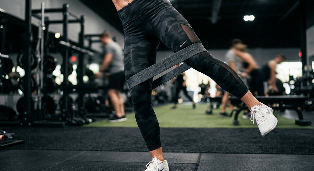 A close-up shot of an athlete's legs in high-performance gym apparel using resistance bands for glute activation, captured with sharp detail and motion blur.