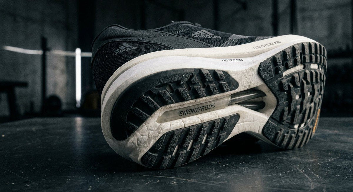 A close-up studio shot of the Adidas Adizero Pacer's outsole and foam structure, showcasing the technical engineering and material textures in a professional, moody setting.