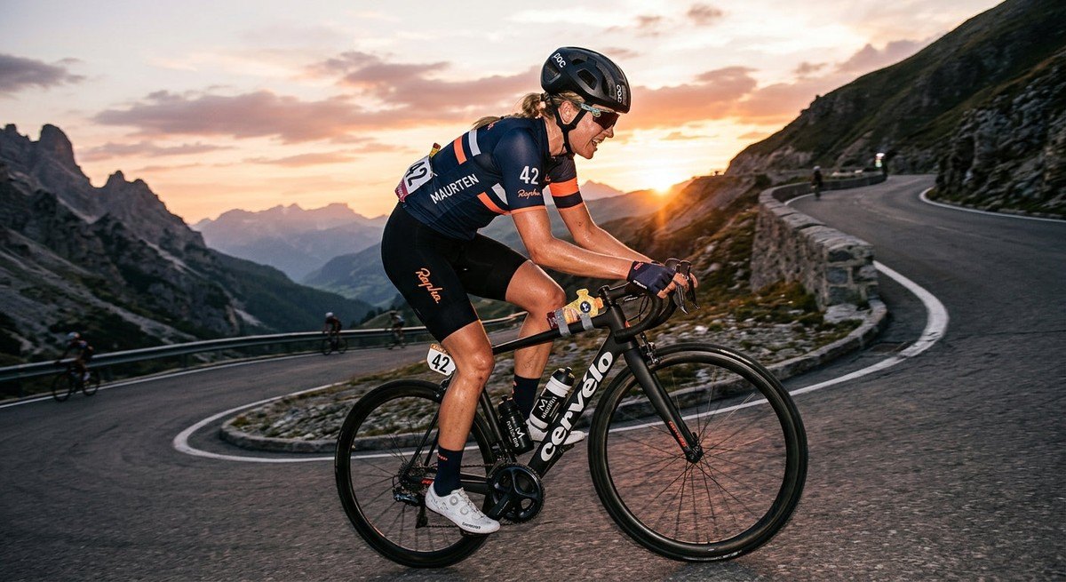 A competitive cyclist climbing a steep mountain pass at sunset, showcasing athletic intensity and the use of advanced nutrition gear.