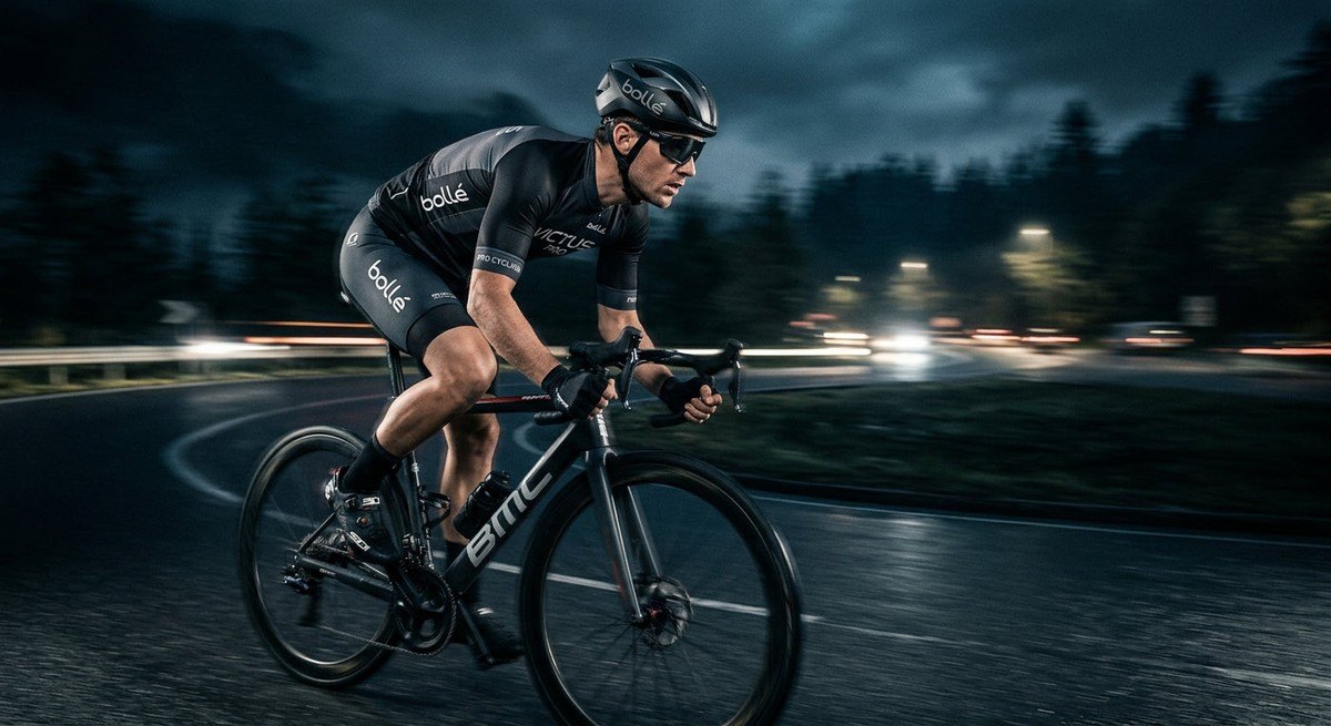 A cyclist in a blurred motion shot wearing the Bollé Victus Pro, highlighting the aerodynamic fit and professional aesthetic against a dark, cinematic background.