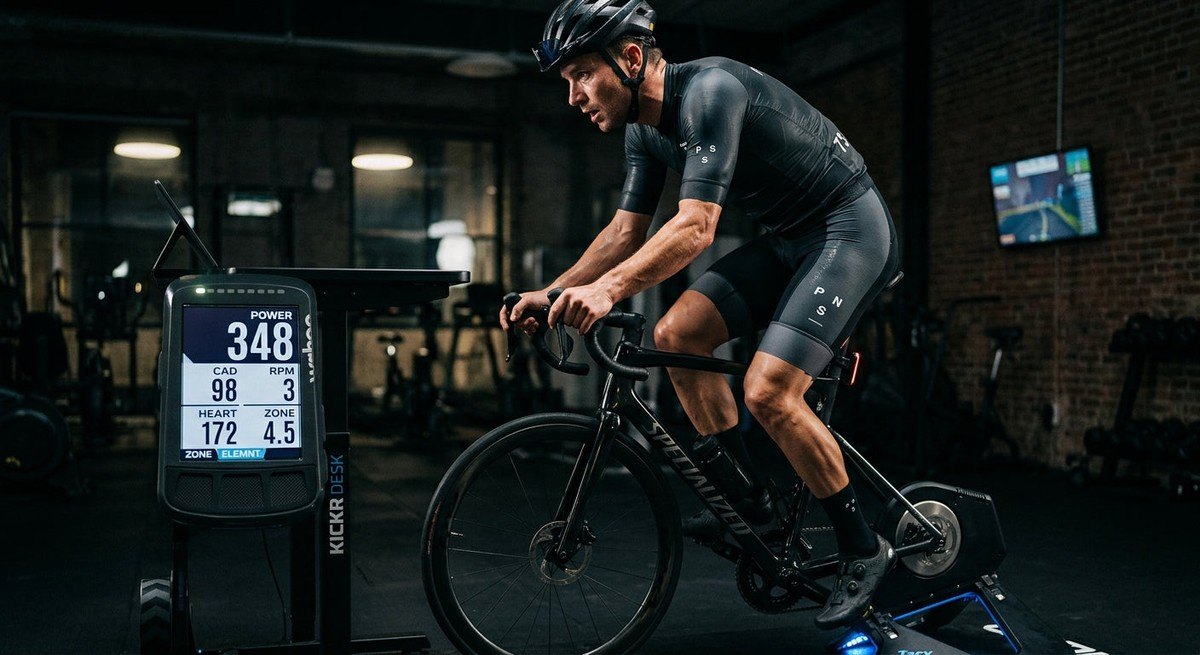 A cyclist training on an indoor smart trainer, showing a digital display of power data with a moody, professional athletic atmosphere.