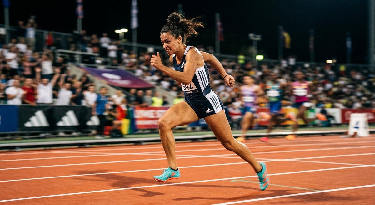 A dynamic action shot of a runner at full speed on a track, wearing the latest Adizero spikes, with motion blur and dramatic stadium lighting capturing the intensity of the race.