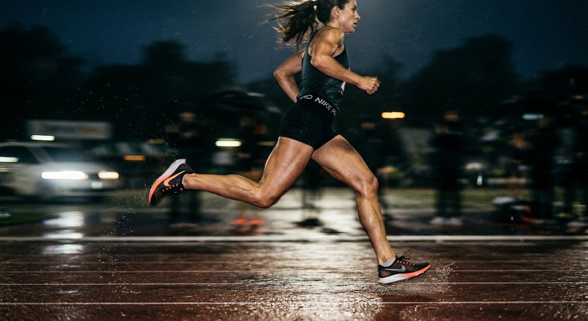 A high-speed action photograph of a runner in motion, captured with a sharp focus on the legs, surrounded by a cinematic, dark atmospheric blur.