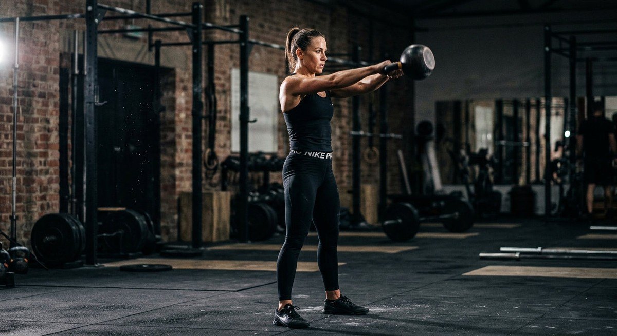 A high-speed photograph of an athlete in a focused training environment, showing the precise biomechanical alignment of a kettlebell swing with dramatic lighting and motion blur.