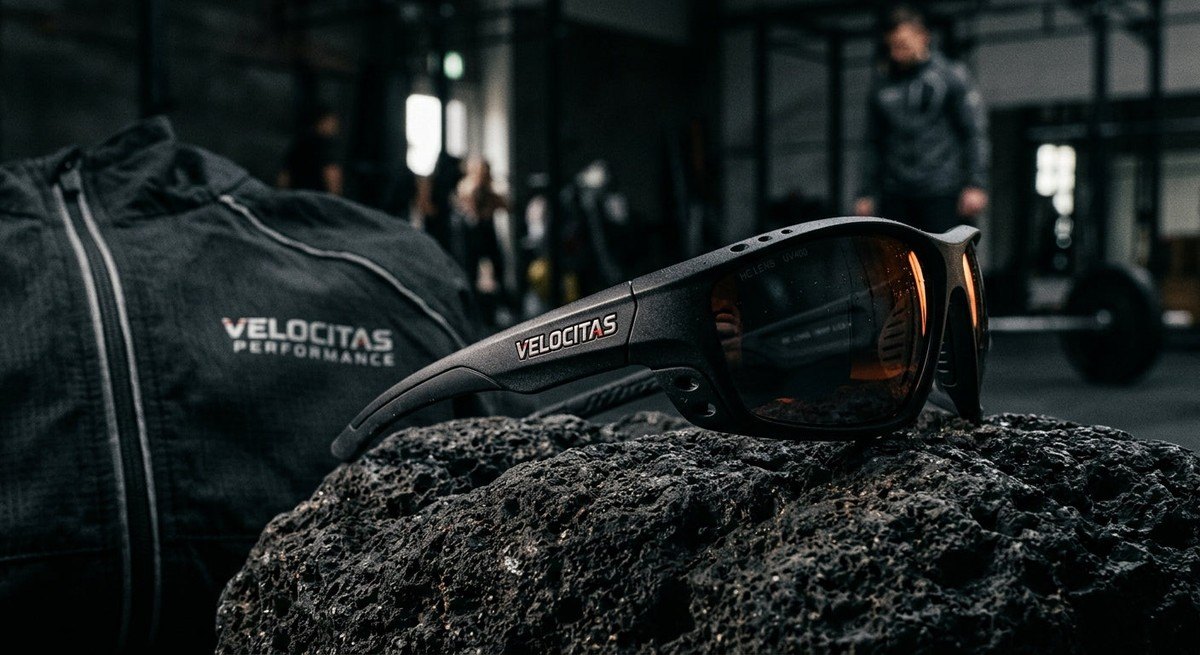 A moody, dramatic shot of athletic eyewear resting on a textured, dark surface with sharp focus on the material quality and branding.