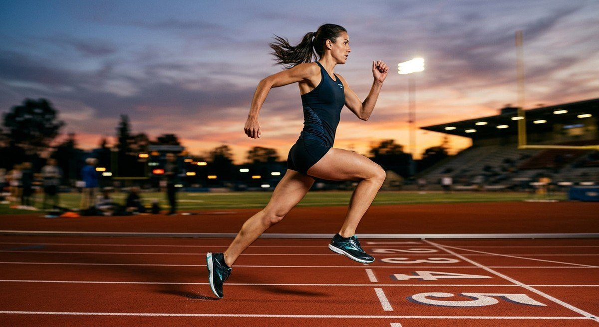 A professional action photo of a runner mid-stride on a track at dusk, capturing the motion blur and the sleek silhouette of the Brooks Ghost 18.