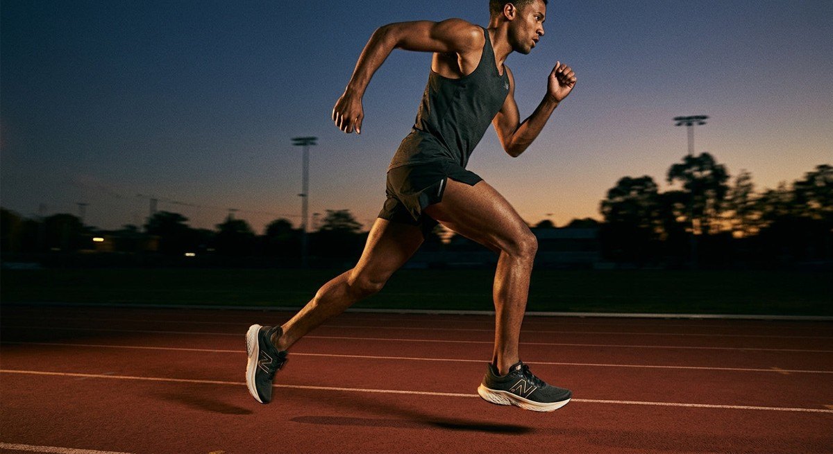 A runner at full speed on a track at dusk, highlighting the sleek silhouette and high-performance design of the New Balance 1080 v16.