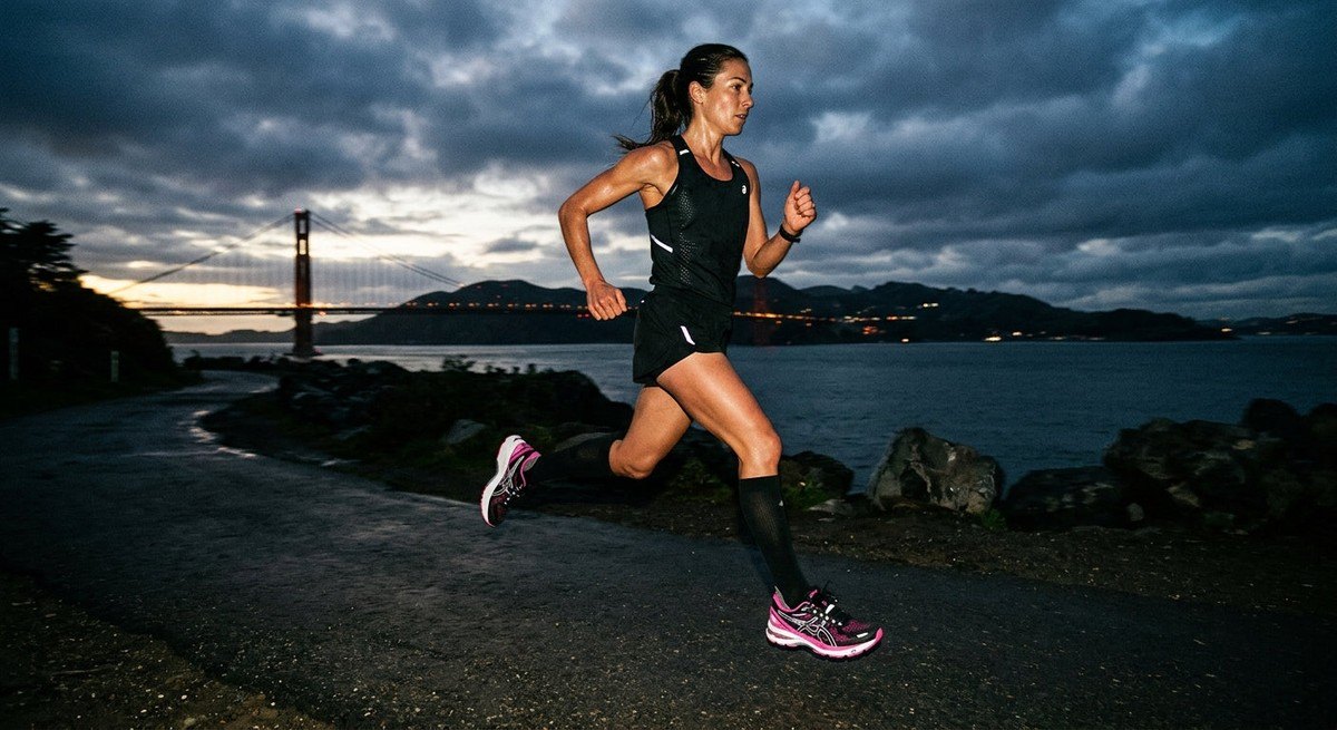 A runner at full stride wearing the ASICS Gel-Kayano 12.1 VANDYTHEPINK, captured in moody, high-contrast lighting.