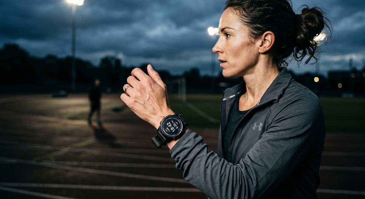 A side-profile view of a runner's wrist featuring the Vallon Watchtower, set against a moody, blurred track background with cinematic high-contrast lighting.