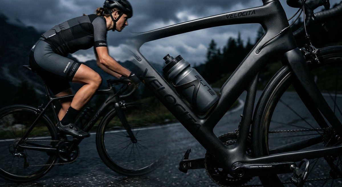 A sleek aero bottle mounted on a carbon fibre bike frame, set against a moody, dramatic background with professional athletic lighting.