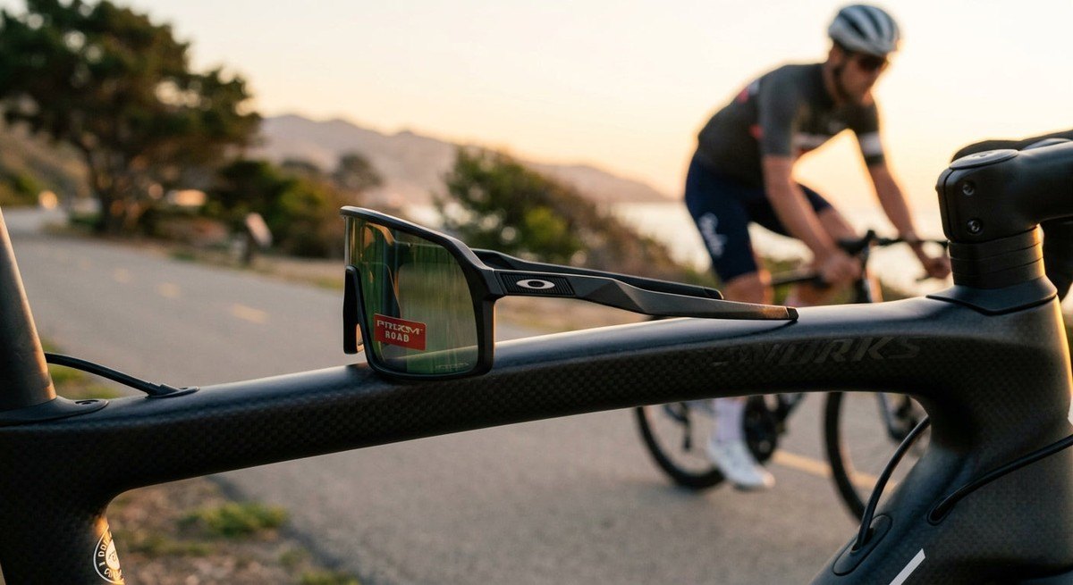 A sleek side profile shot of the Oakley Sutro Lite Sweep sunglasses resting on a carbon fibre bike frame, highlighting the ergonomic design.