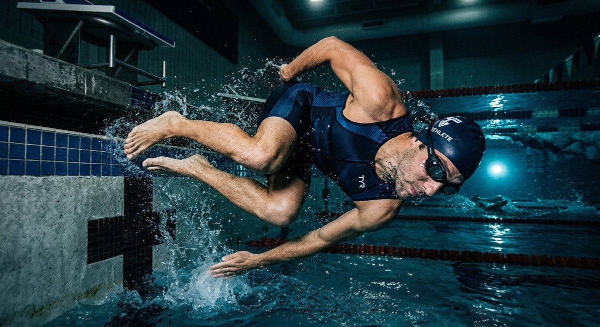 A triathlete performing a flip turn in a pool, showcasing the sleek, low-profile design of the Smart Swim 2 goggles in a moody, high-contrast environment.