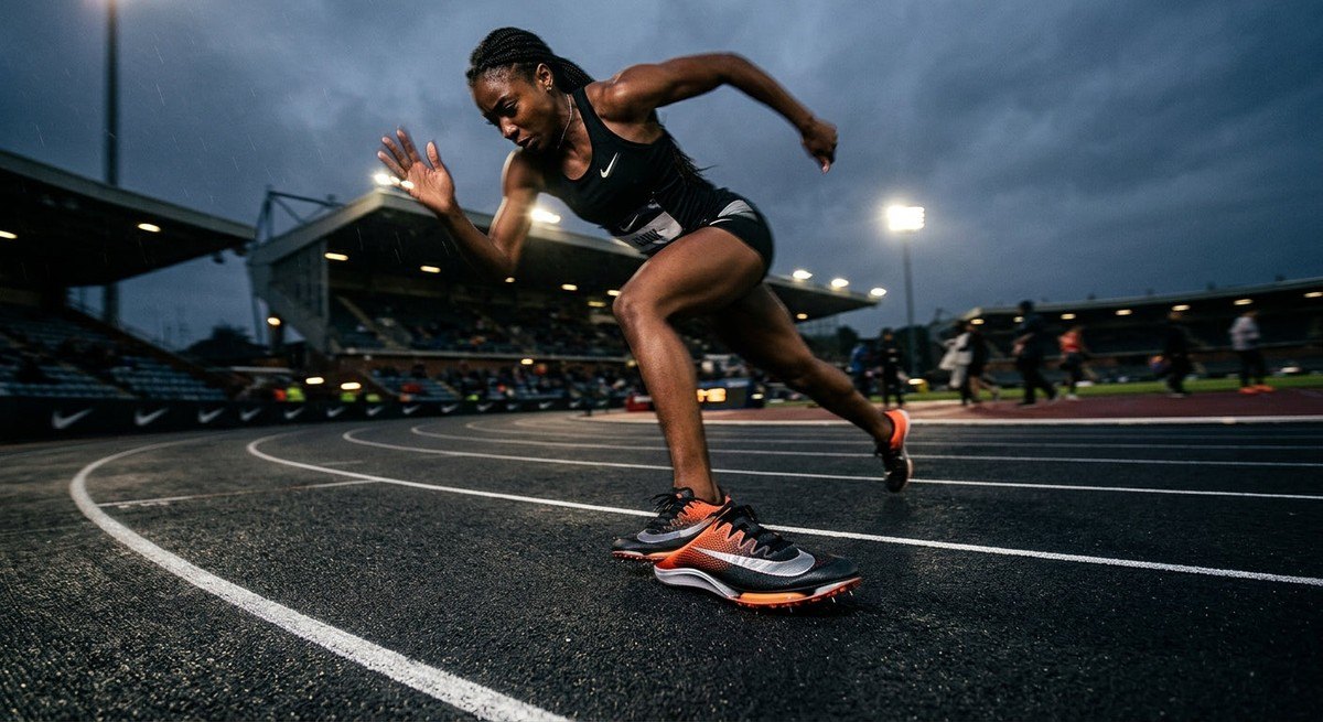 A wide-angle action shot of an athlete sprinting on a dark, moody track, with the focus sharp on the footwear to emphasise the sleek, aggressive geometry of the shoe.