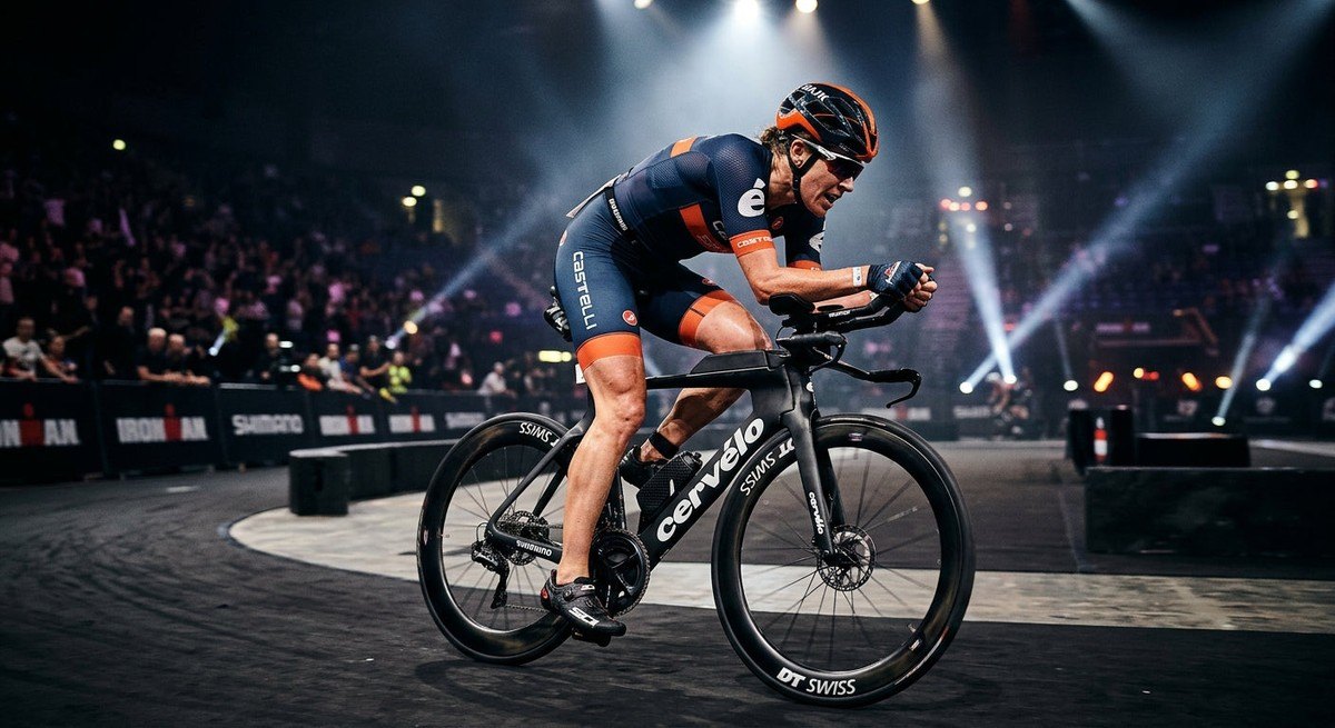 Action shot of a female cyclist in a professional triathlon position, showing intense focus and sharp textures under dramatic arena spotlights
