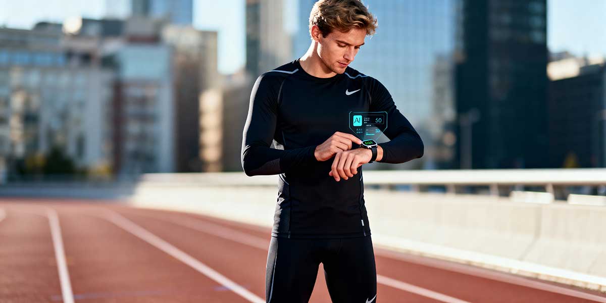 A full length photo of a male athlete checking his biometric data on a smart watch at an outdoor track.