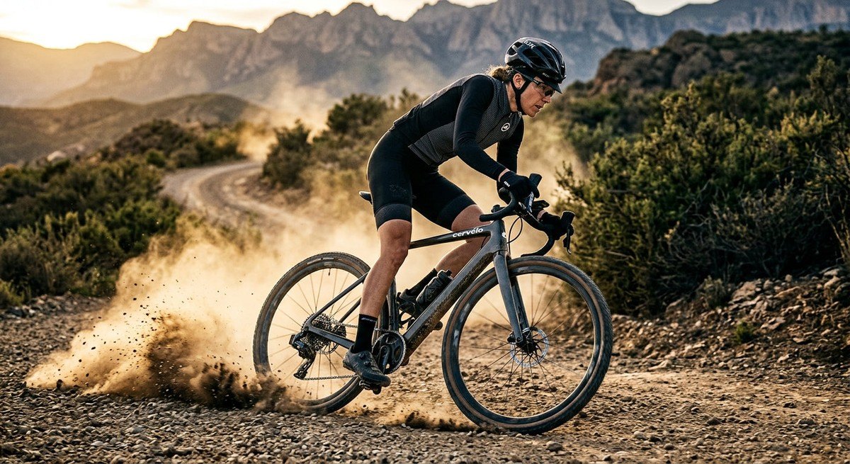 An action shot of a gravel bike kicking up dust on a trail, emphasising the aggressive tread and motion blur of the wheels.