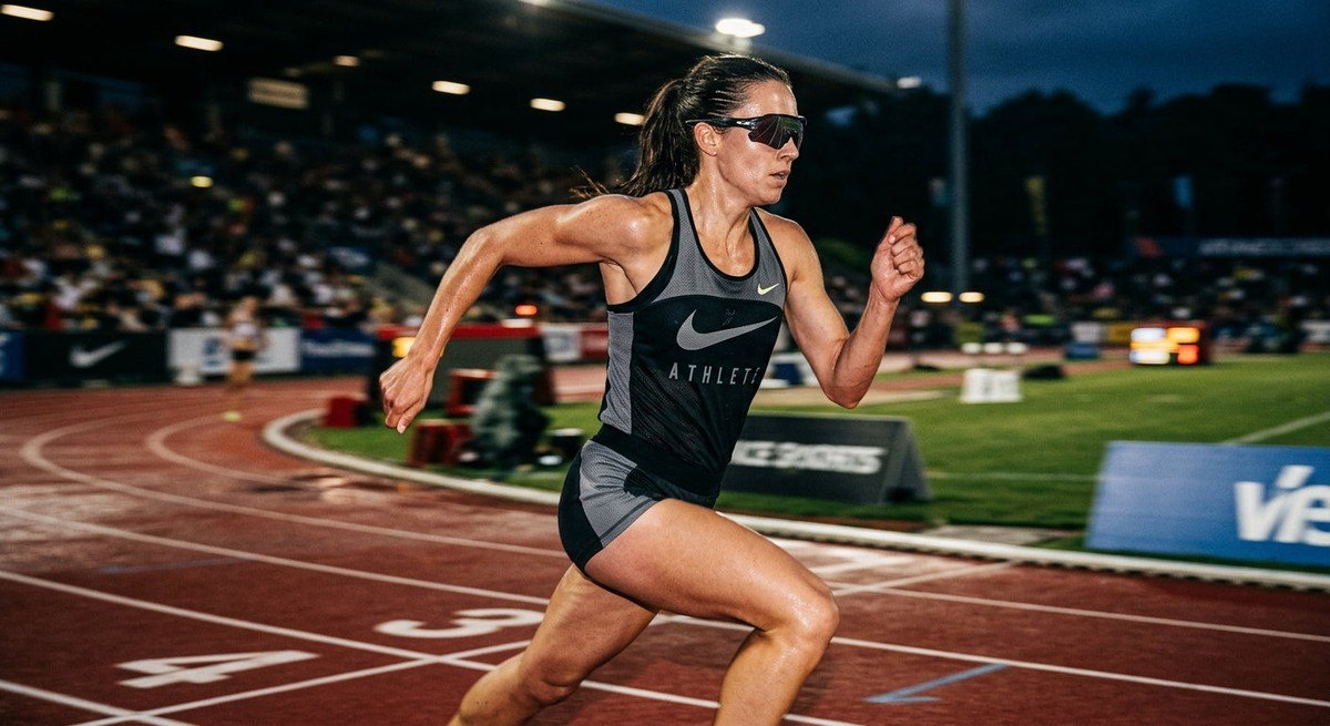 An athlete in motion wearing high-performance sunglasses, capturing the realistic textures of the frame and the intense contrast of the lighting against a blurred track background.