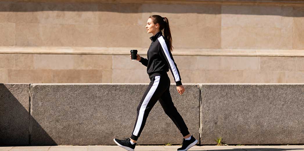 A full length shot of a female athlete walking with a black coffee to avoid hidden coffee shop sugars.
