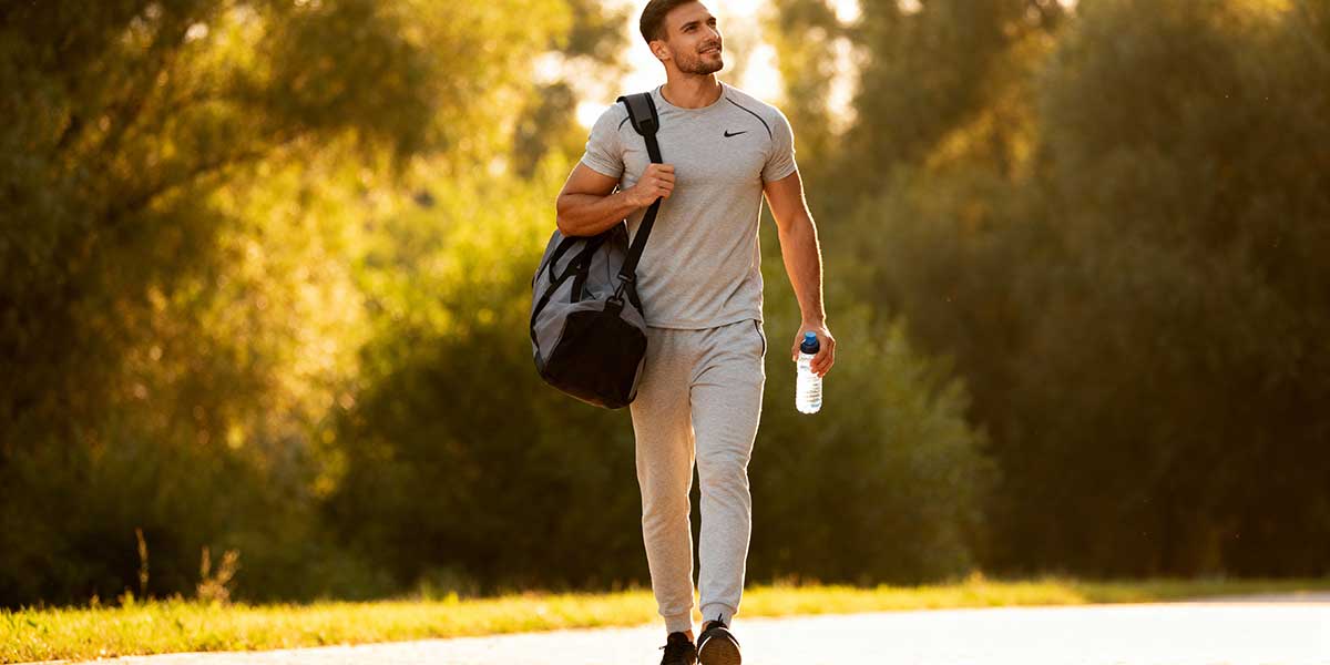 A full length photo of an athlete walking with a gym bag, representing a consistent and sustainable approach to long-term health.