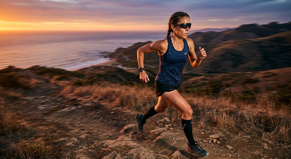 Athletic action shot of a runner wearing technical eyewear during a sunset training session, featuring motion blur in the background and dramatic cinematic lighting on the athlete's face.