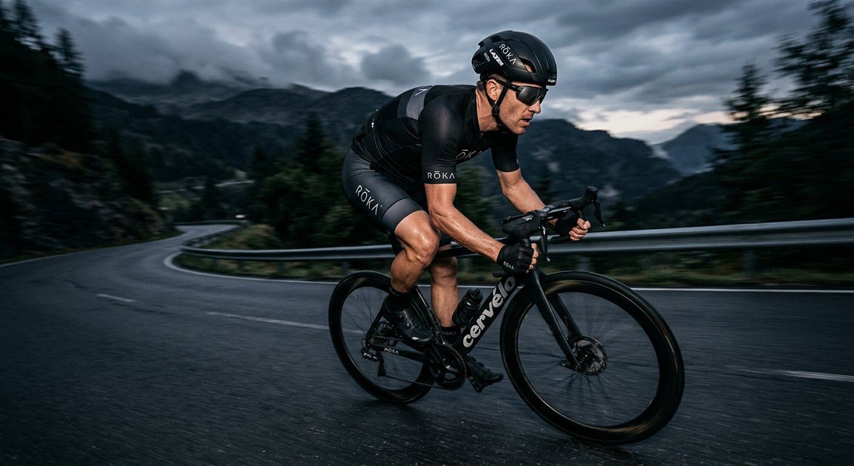 Athletic motion blur shot of a cyclist wearing ROKA Ion sunglasses, highlighting the aerodynamic frame design and ergonomic fit in a moody, high-contrast environment.