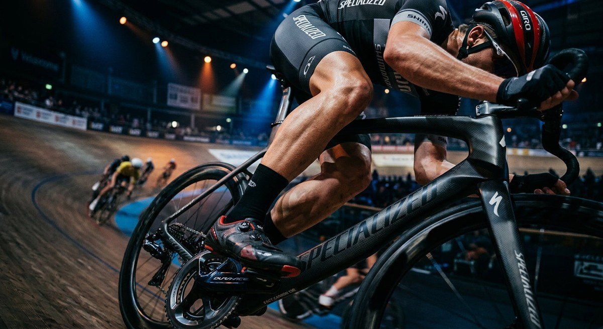 Close-up of a carbon fibre bike frame under dramatic arena lighting, highlighting the intricate textures and advanced engineering.