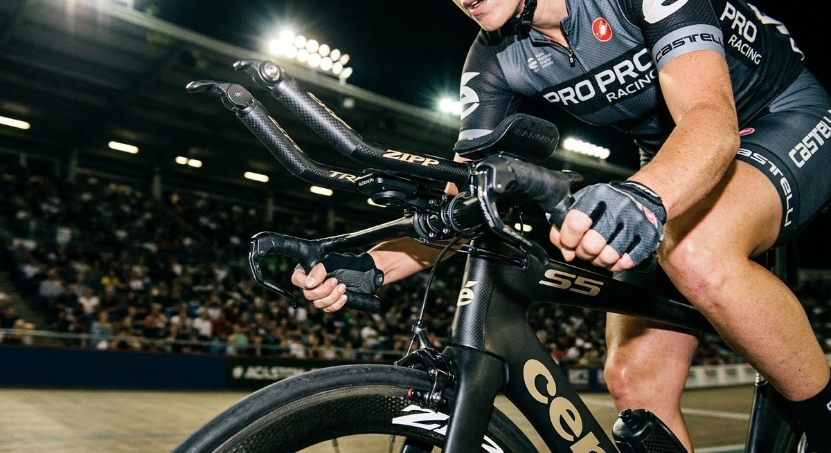 Close-up of a carbon fibre road bike frame featuring high-tech aero bar attachments and professional racing components under dramatic stadium lights.