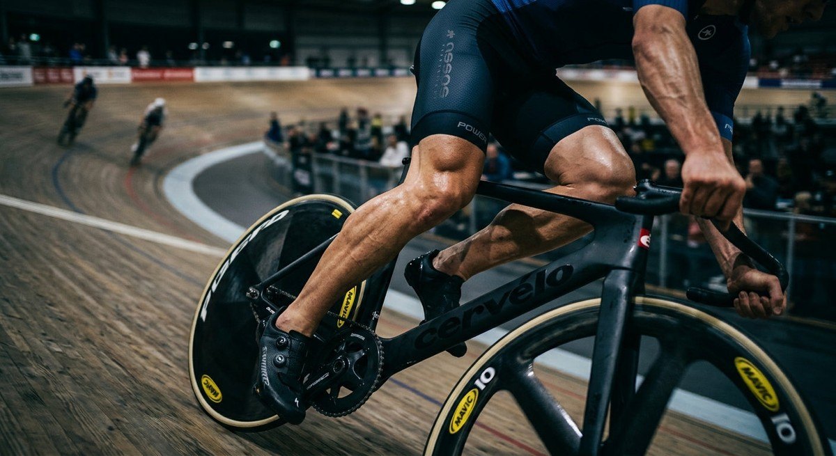 Close-up of a competitive cyclist's legs showcasing muscular definition during an intense sprint on a velodrome track.
