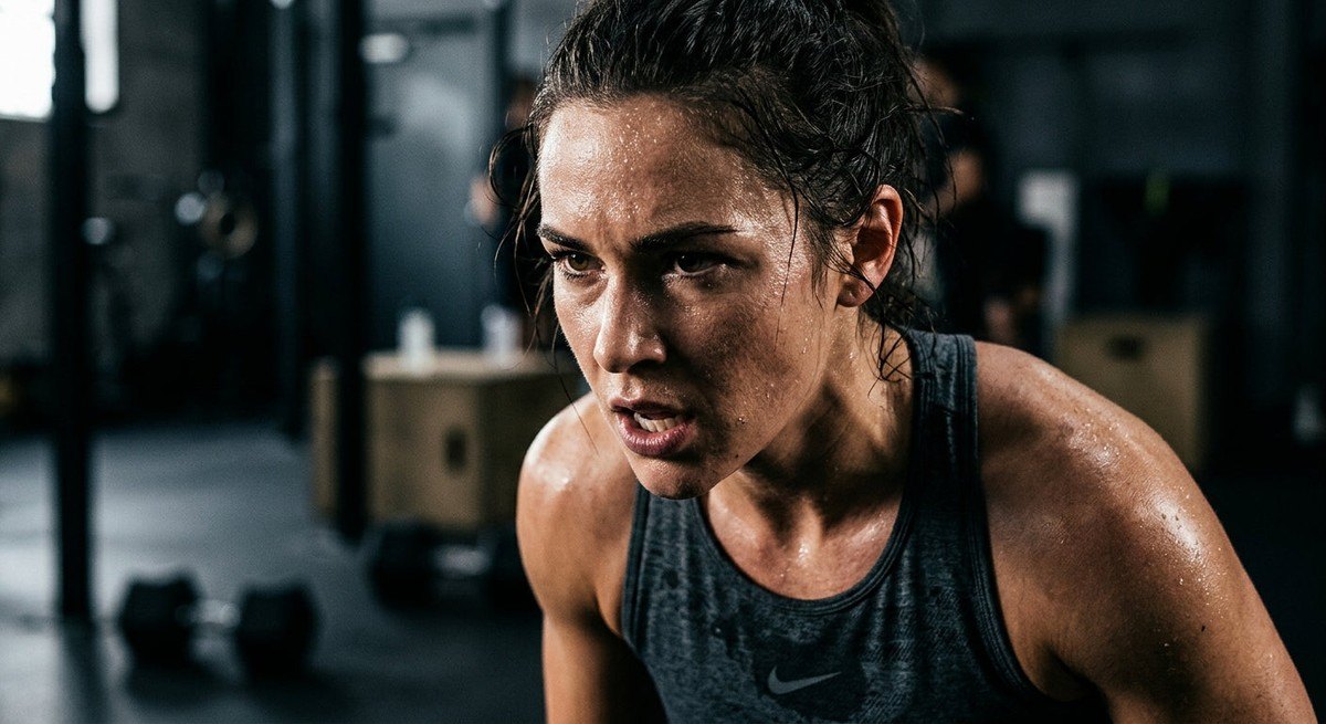 Close-up of a focused athlete's face during an intense interval workout, showing realistic sweat texture and dramatic, high-contrast lighting.