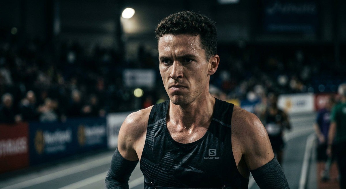 Close-up of a focused marathon runner in a stadium, sweat visible on skin, sharp details with moody low-key lighting highlighting intense determination.