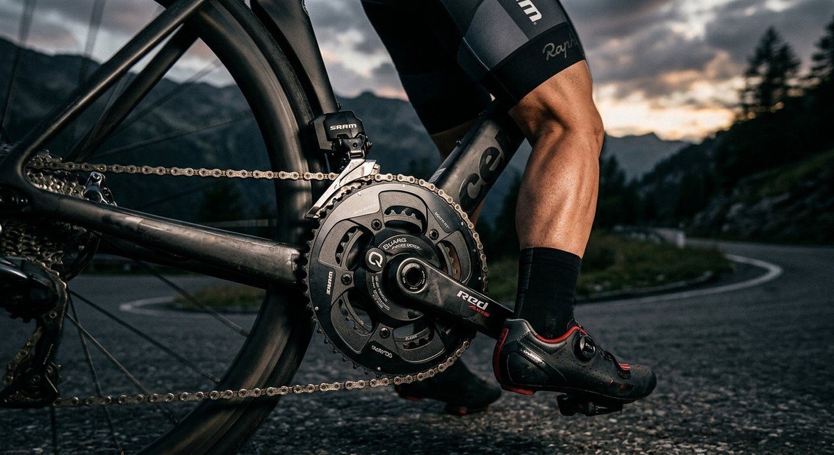 Close-up of a high-end bicycle crank-based power meter, highlighting the metallic texture and technical design in dramatic lighting.