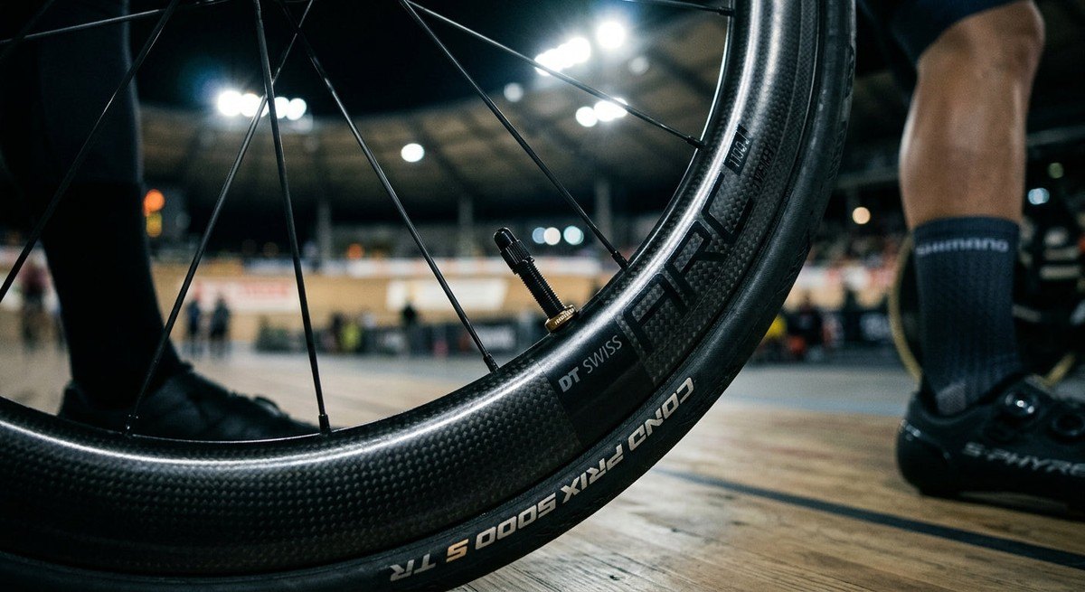 Close-up of a high-performance bicycle wheel showing the intricate detail of a tyre valve and carbon rim under dramatic stadium lighting.